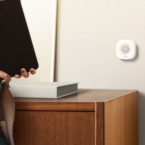 Person holding a book next to a wall-mounted motion sensor.