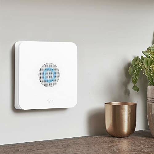 Smart home alarm siren on wall with plant and cup nearby.